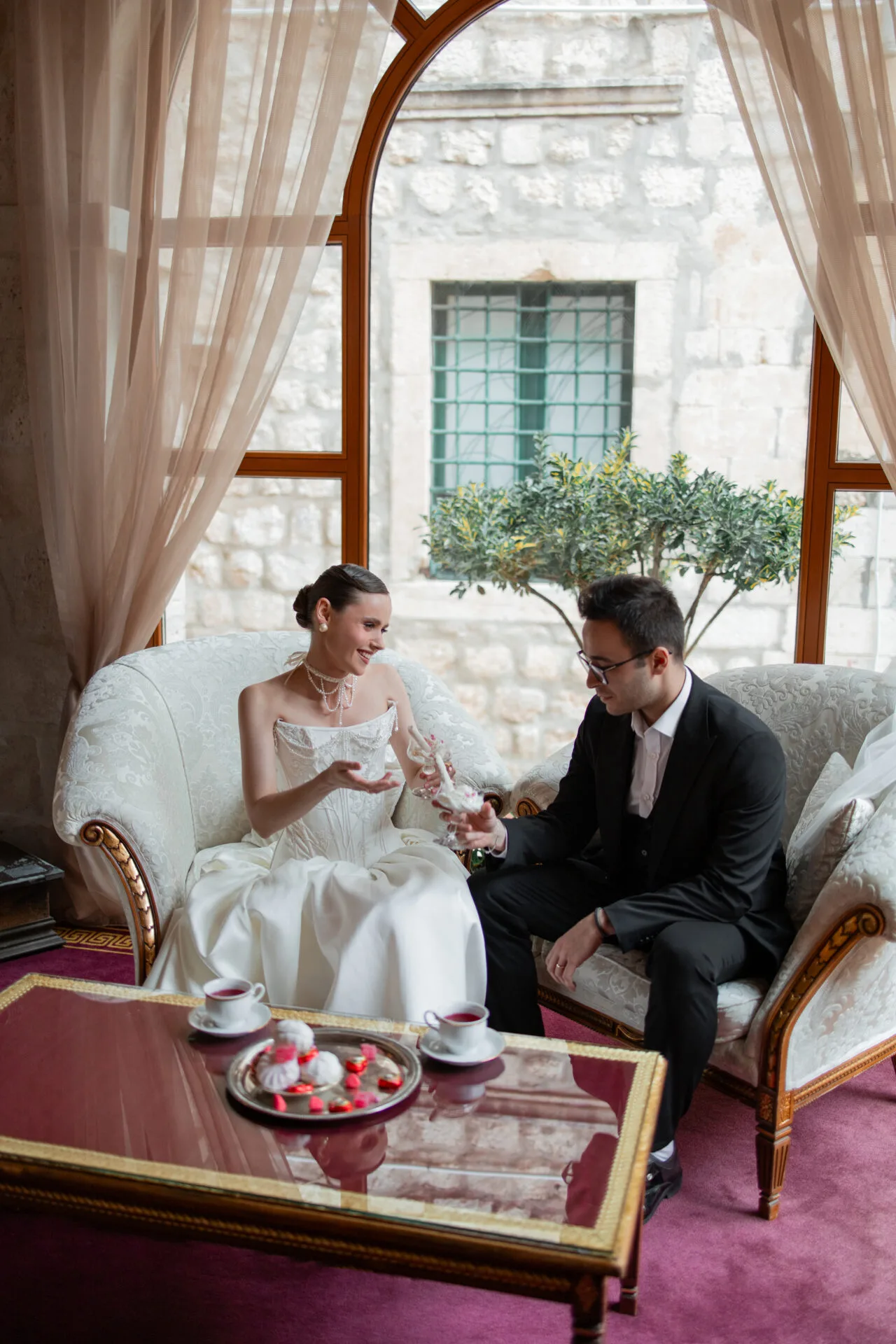 Newlyweds with champagne in an armchair by a panoramic window