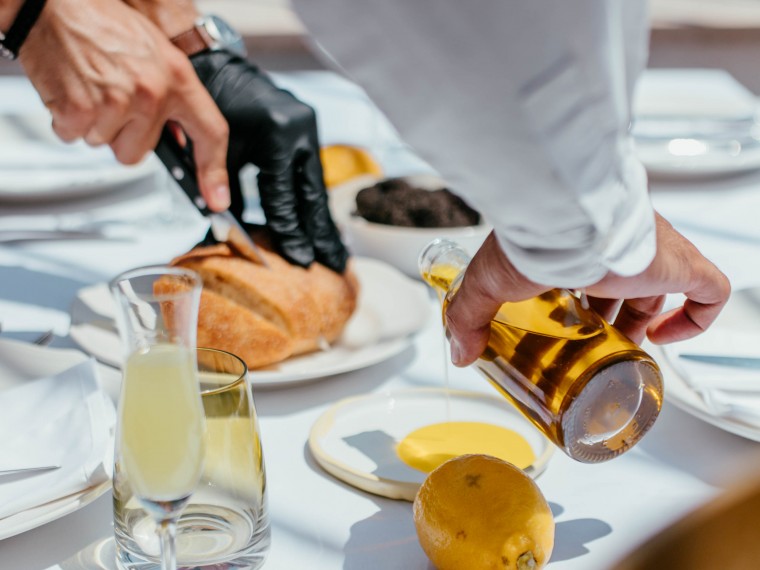 Chef slices bread while pouring olive oil at table