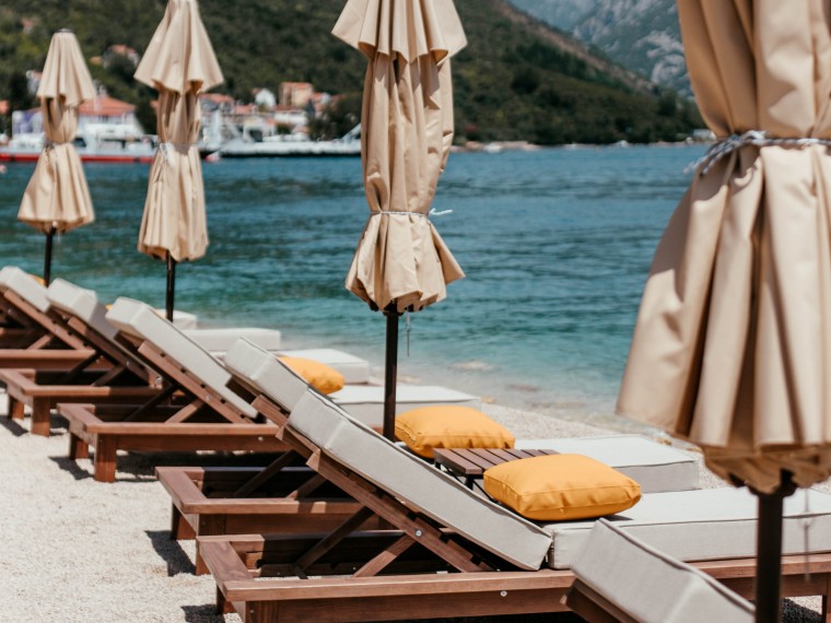 Beach loungers and closed umbrellas beside turquoise coastal water